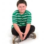 an image of a boy in a green shirt sitting cross legged on the floor