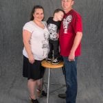 an image of a mother and father standing around their son who is standing on a stool
