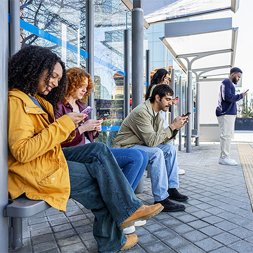 People waiting outside for bus or train, sitting on a bench