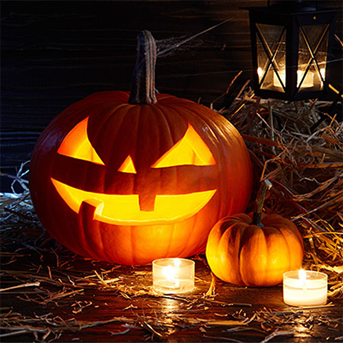 a jack-o-lantern light up by a candle with a small pumpkin sitting next to it